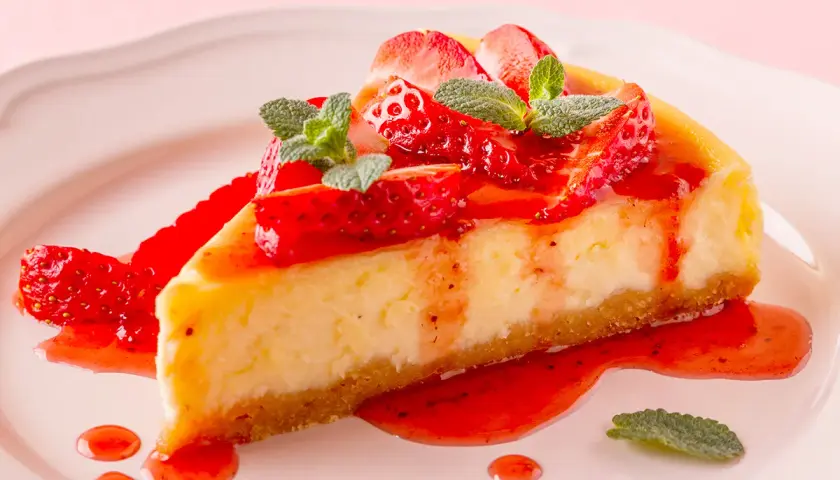 Deliciosa tarta de queso con fresas frescas y salsa de fresa, decorada con hojas de menta.