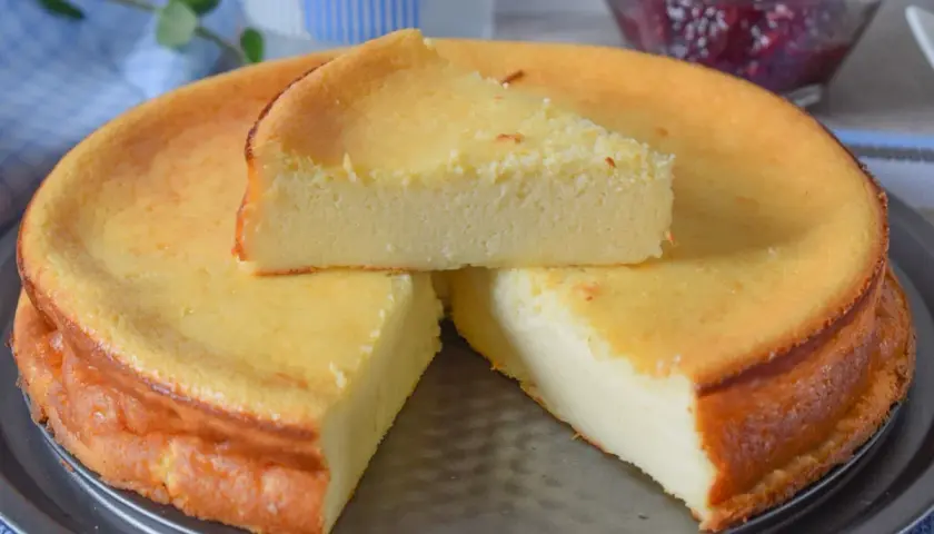 Tarta de queso al horno, dorada y esponjosa, con una porción servida. Un postre casero perfecto.