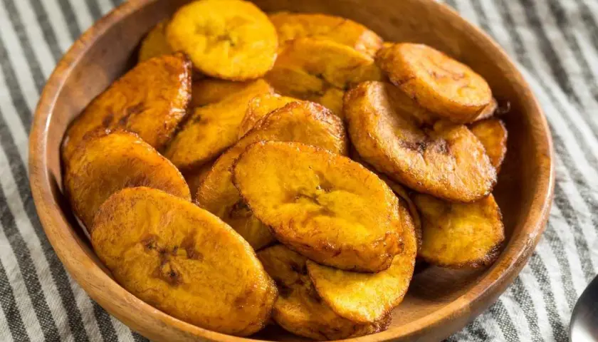 Un tazón de madera lleno de crujientes rodajas de plátano frito, doradas y listas para disfrutar.