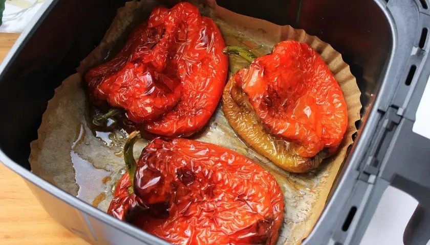 Tres pimientos rojos asados en freidora de aire, con piel arrugada y jugosos, listos para disfrutar.