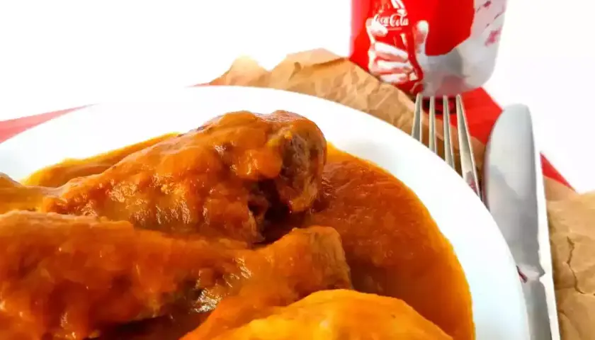 Sabroso pollo a la Coca Cola en un plato blanco, acompañado de cubiertos y una lata de Coca Cola.