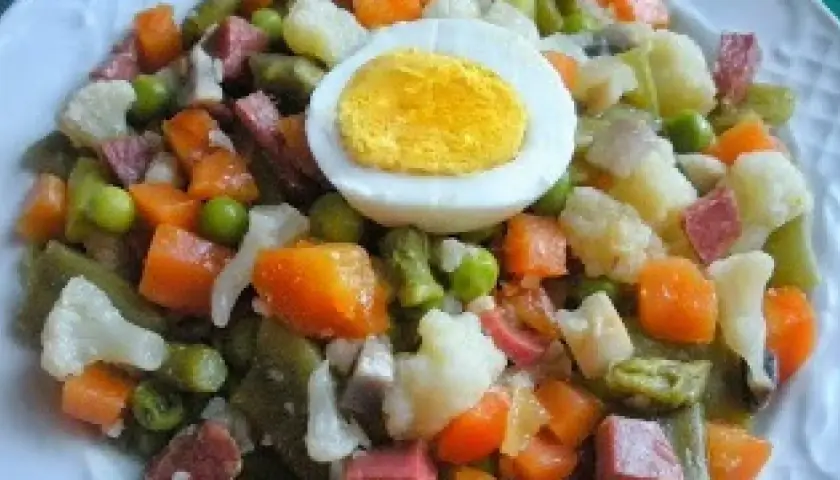 Un plato de menestra de verduras con trozos de zanahoria, guisantes, judías verdes, coliflor y patata, coronado con medio huevo duro.