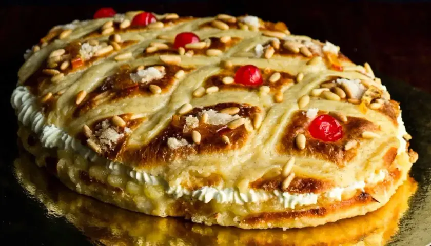 Deliciosa coca de Sant Joan rellena de crema, decorada con piñones, cerezas rojas y azúcar.
