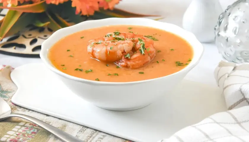 Deliciosa crema de marisco servida en un cuenco blanco, coronada con gambas y perejil picado.