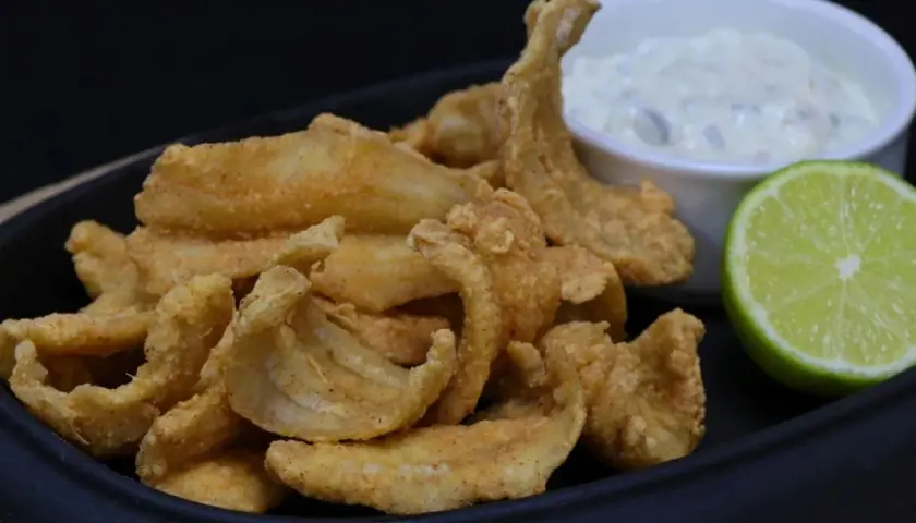 Crujiente bacaladilla frita servida con una salsa cremosa y una rodaja de lima.