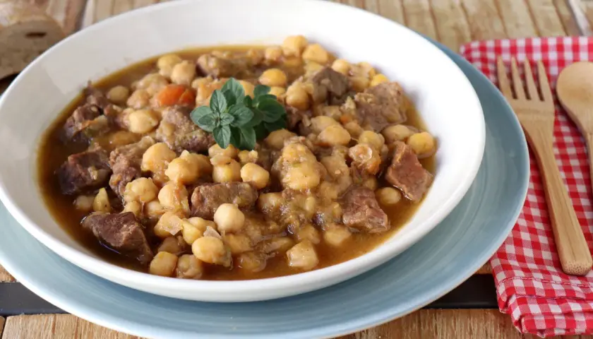 Un plato humeante de garbanzos con carne, perfecto para una receta de garbanzos tradicional. Decorado con una ramita de hierbas frescas.