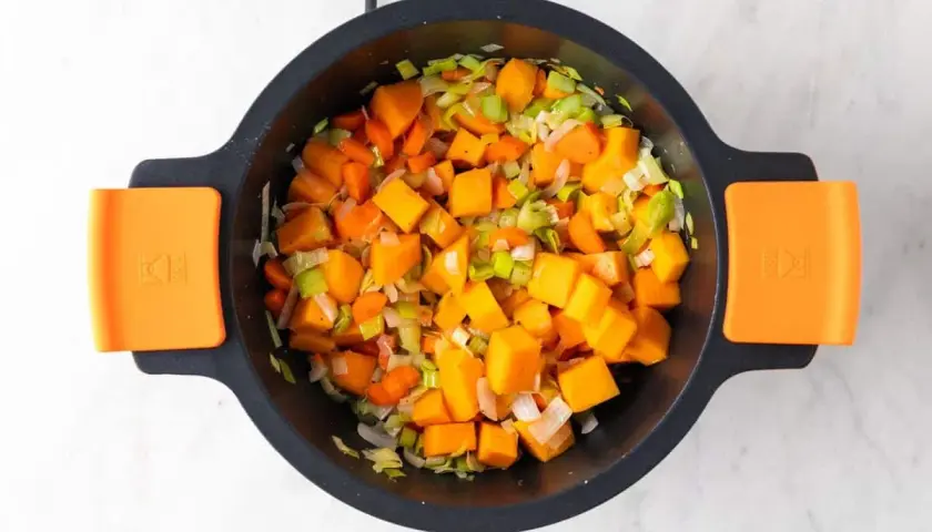 Trozo de calabaza, zanahoria y puerro picados en una olla, listos para hacer una deliciosa crema de verduras.