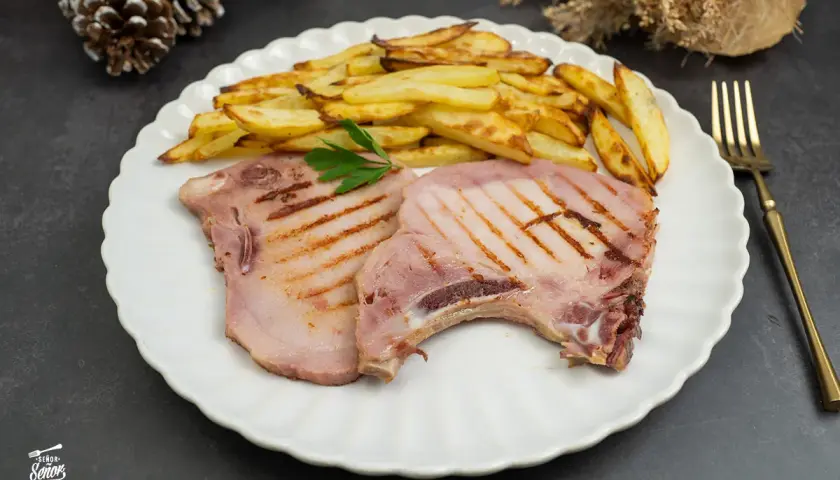 Dos chuletas de sajonia a la parrilla con patatas fritas y perejil en un plato blanco.