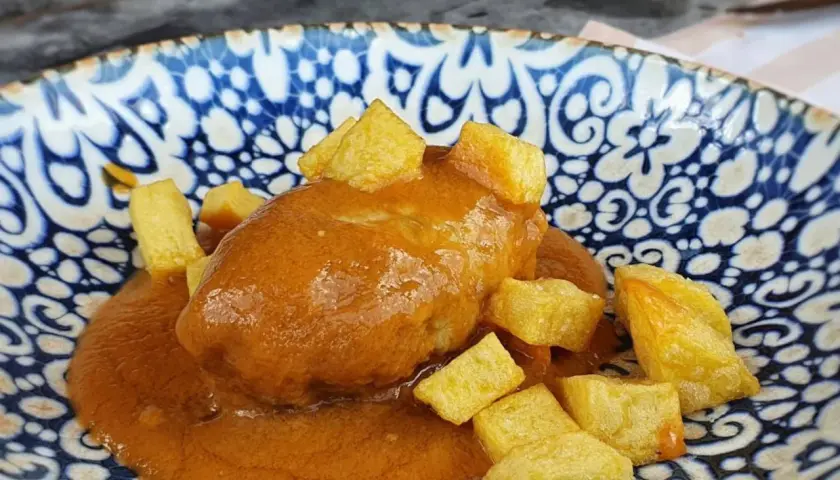 Rollo de bonito en salsa con patatas fritas, servido en un plato azul y blanco.