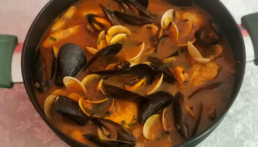 Caldereta de pescado humeante en una olla, repleta de mejillones, almejas y trozos de pescado en una rica salsa roja.