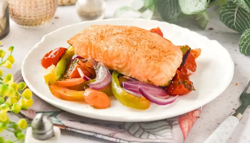 Delicioso salmón al horno con verduras coloridas: tomates, pimientos y cebolla morada. Un plato saludable y lleno de sabor.