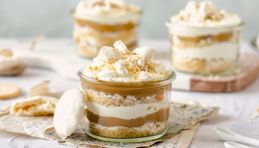 Postres en vaso con capas de galleta, crema y dulce de leche. Coronados con merengue y un toque de polvito canario.
