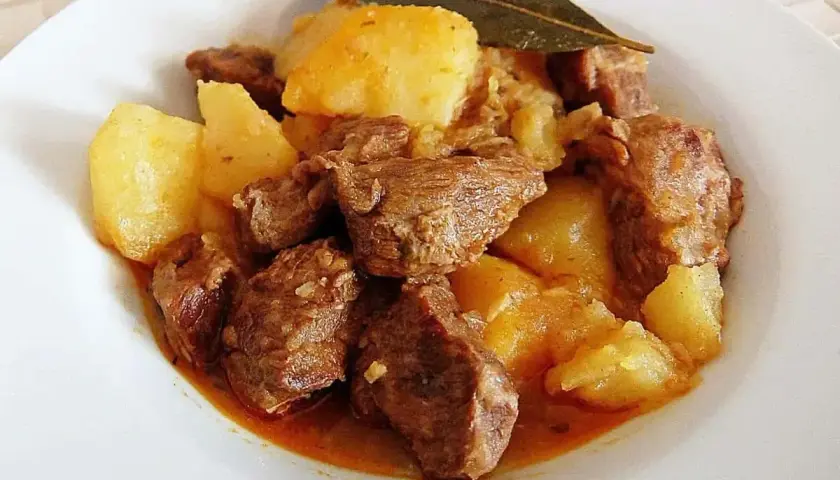 Plato de morcillo de ternera estofado con patatas y una hoja de laurel.