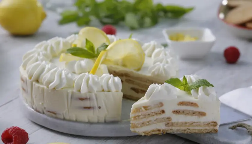 Deliciosa tarta de limón sin horno, con capas de galleta y crema, decorada con merengue, rodajas de limón y menta.