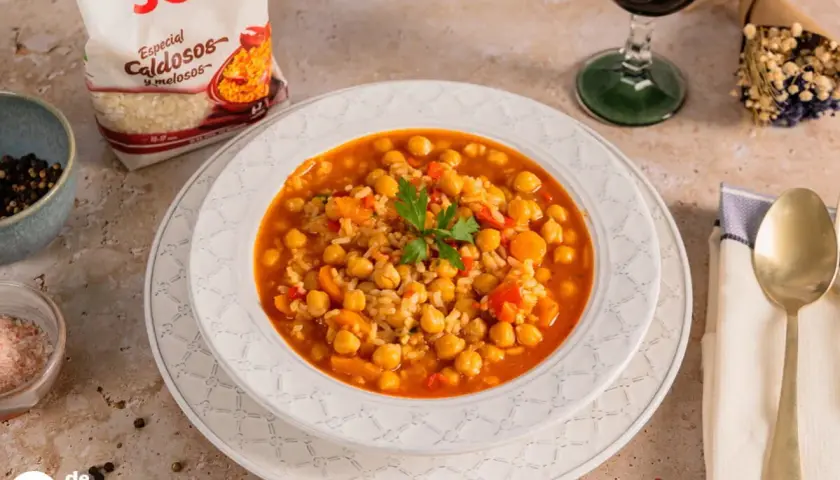 Plato de garbanzos con arroz, pimientos y zanahoria, decorado con perejil. Acompañado de una copa de vino tinto y una bolsa de arroz SOS.