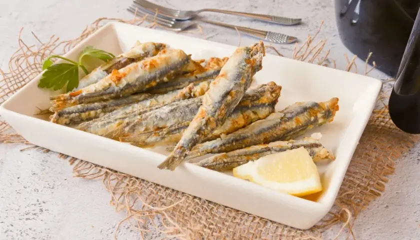 Boquerones crujientes en freidora de aire, servidos en plato blanco con limón y perejil.