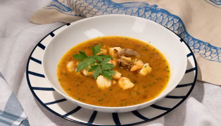 Un plato de sopa de pescado con trozos de marisco, gambas y mejillones, decorado con perejil fresco.