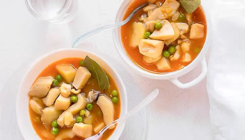 Dos cuencos de sepia con patatas y guisantes en salsa. Un vaso de agua al lado.