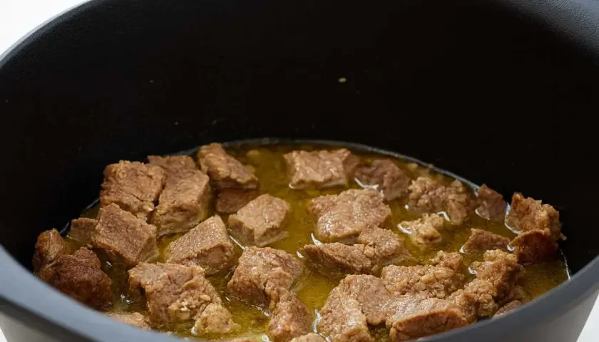 Trozos de magro con tomate cocinándose en una olla negra.