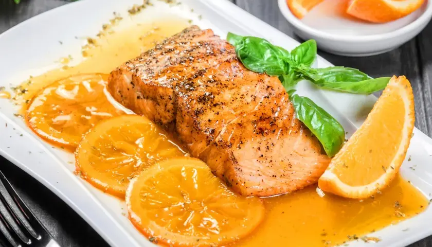 Delicioso salmón a la naranja, servido con rodajas de naranja y hojas de albahaca fresca.