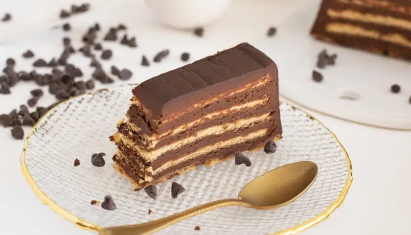 Rebanada de tarta de galletas de la abuela, con capas de galleta y chocolate, decorada con chispas de chocolate y una cuchara dorada.