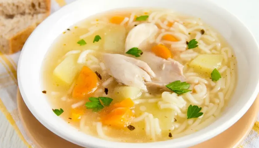 Un reconfortante plato de sopa de pollo con fideos, trozos de zanahoria y patata, adornado con perejil fresco.