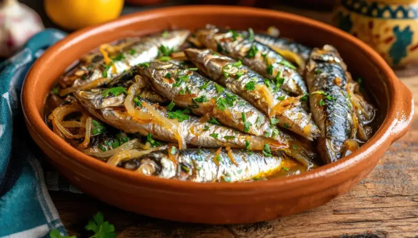 Sardinas en escabeche, un plato tradicional español, servido en una cazuela de barro con cebolla y perejil picado.