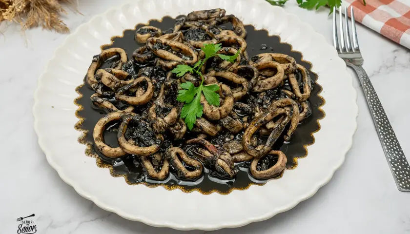 Calamares en su tinta, una receta tradicional servida en un plato blanco con un tenedor y perejil fresco.