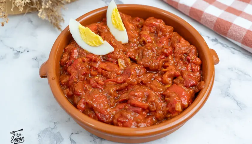 Un sabroso asadillo manchego en cazuela de barro, decorado con gajos de huevo cocido.
