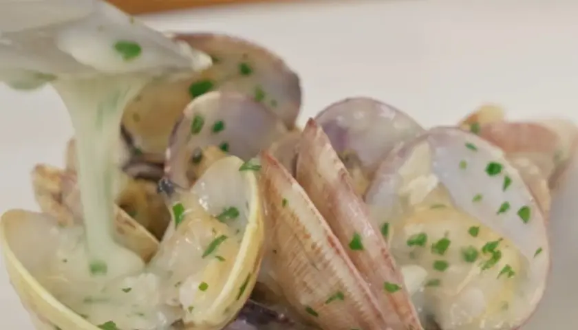 Almejas en salsa verde, con una cremosa salsa blanca y perejil picado, listas para ser servidas.