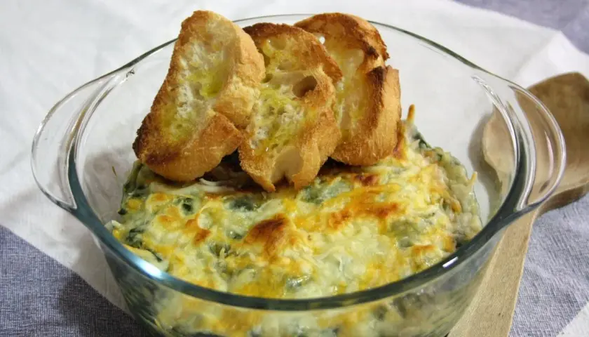 Delicioso plato de espinacas con bechamel gratinado, coronado con tostadas de pan.