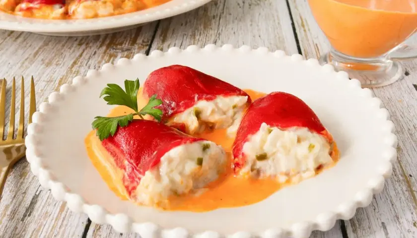 Pimientos del piquillo rellenos de bacalao, cubiertos en una cremosa salsa naranja, adornados con perejil fresco.