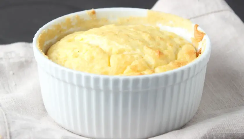 Un esponjoso soufflé de patatas recién horneado en un ramekin blanco, listo para ser disfrutado.