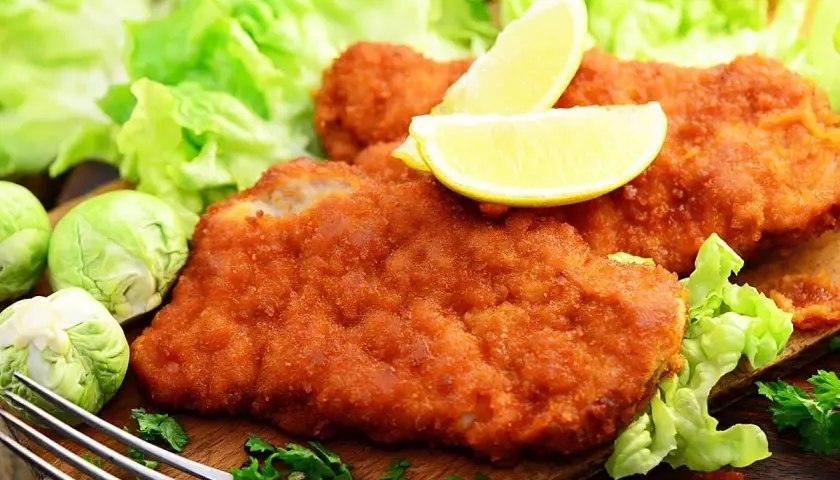 Dos filetes empanados dorados, servidos con lechuga fresca, limones y coles de Bruselas. Un plato delicioso y crujiente.