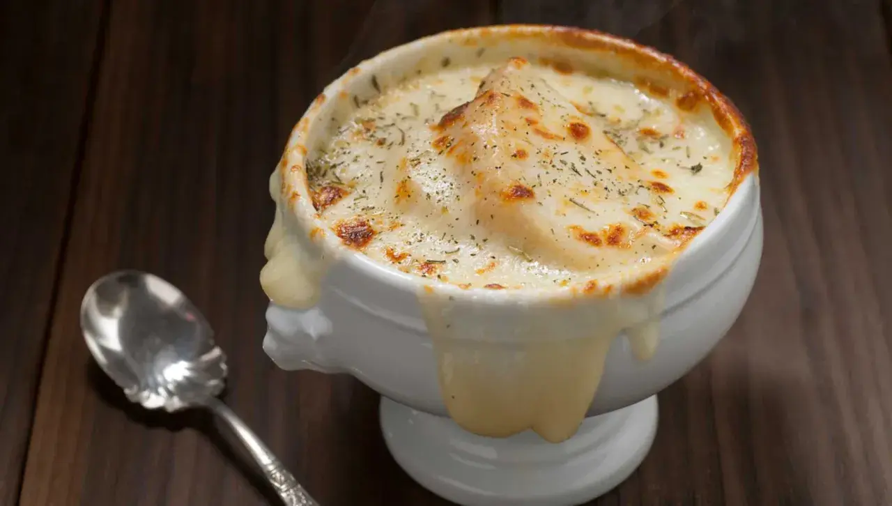 Sopa de cebolla gratinada, con queso derretido y hierbas, humeante y deliciosa, lista para ser disfrutada con una cuchara.