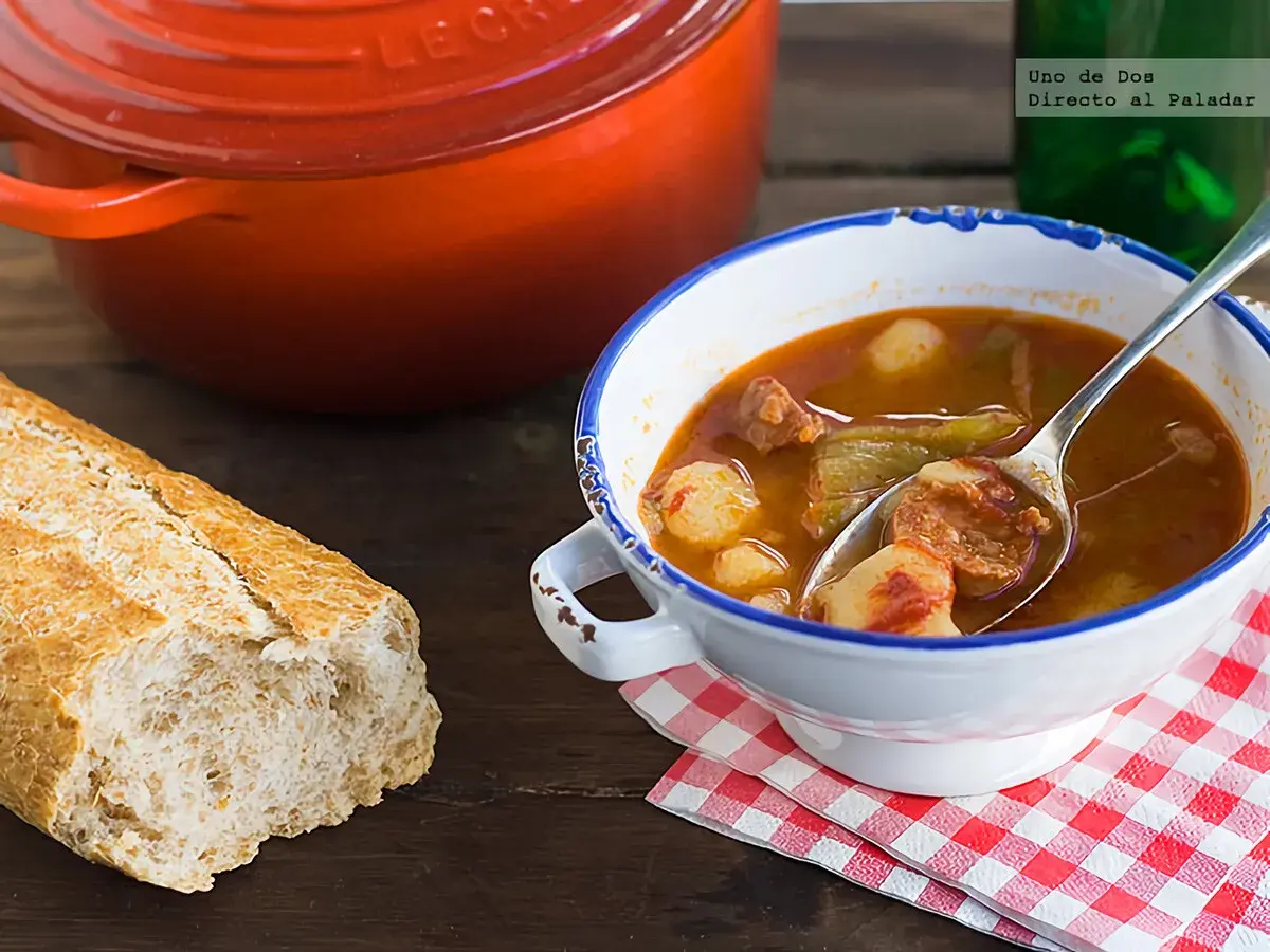 Un plato humeante de patatas a la riojana, con chorizo y pimientos, acompañado de pan rústico y una olla roja.
