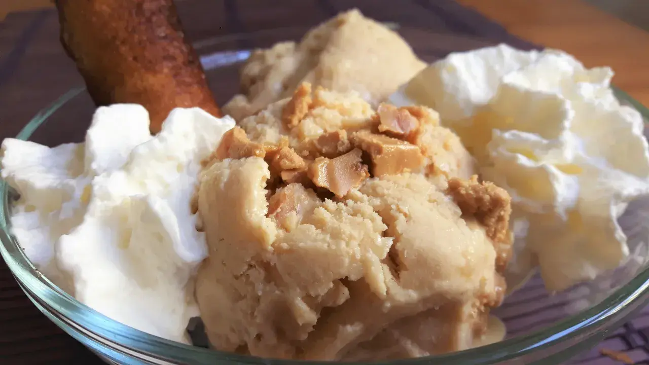 Delicioso helado de turrón con trozos crujientes, acompañado de nata montada y un bizcocho dorado.