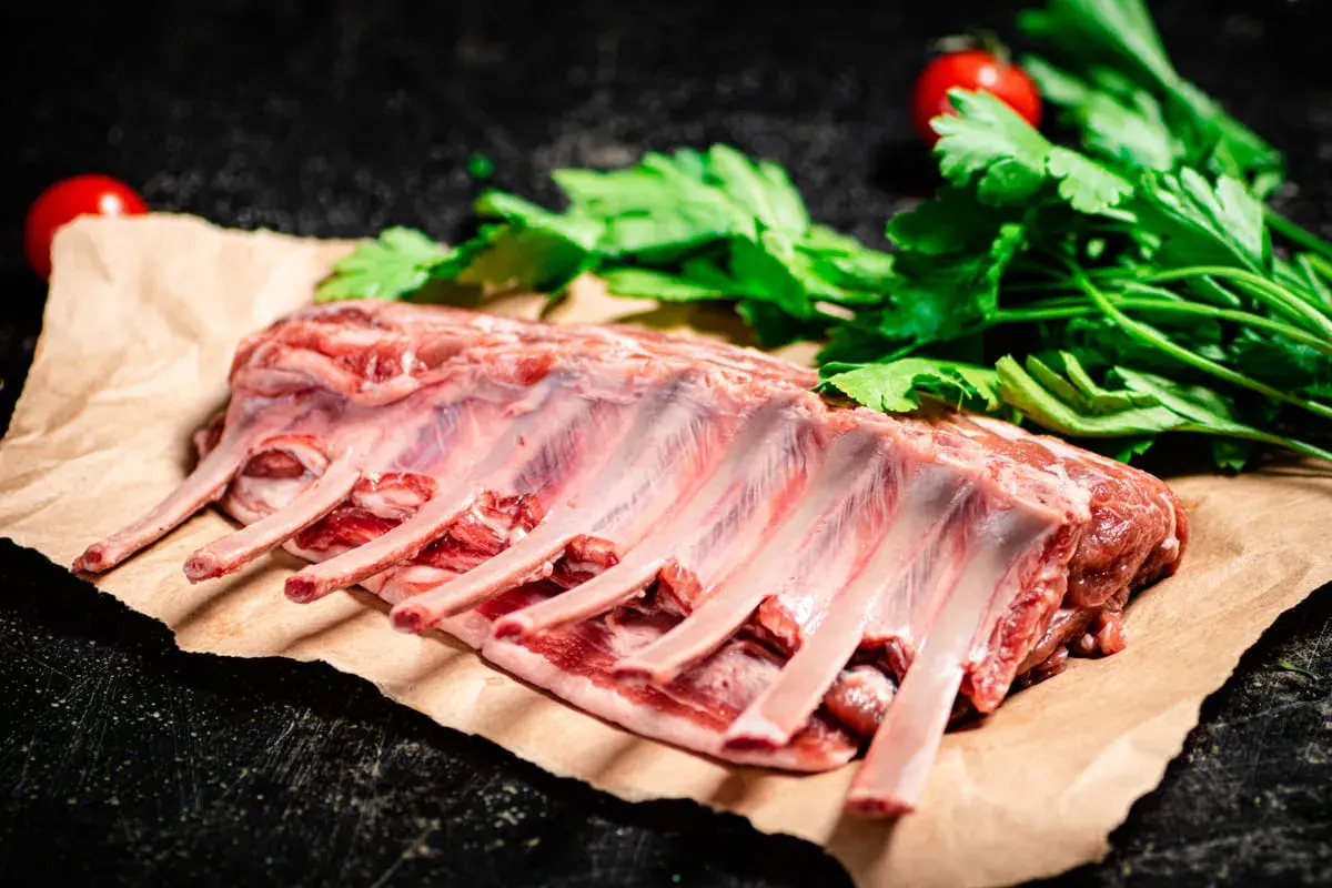 Costillar de cordero crudo, listo para preparar un delicioso cordero al chilindrón con perejil y tomates.