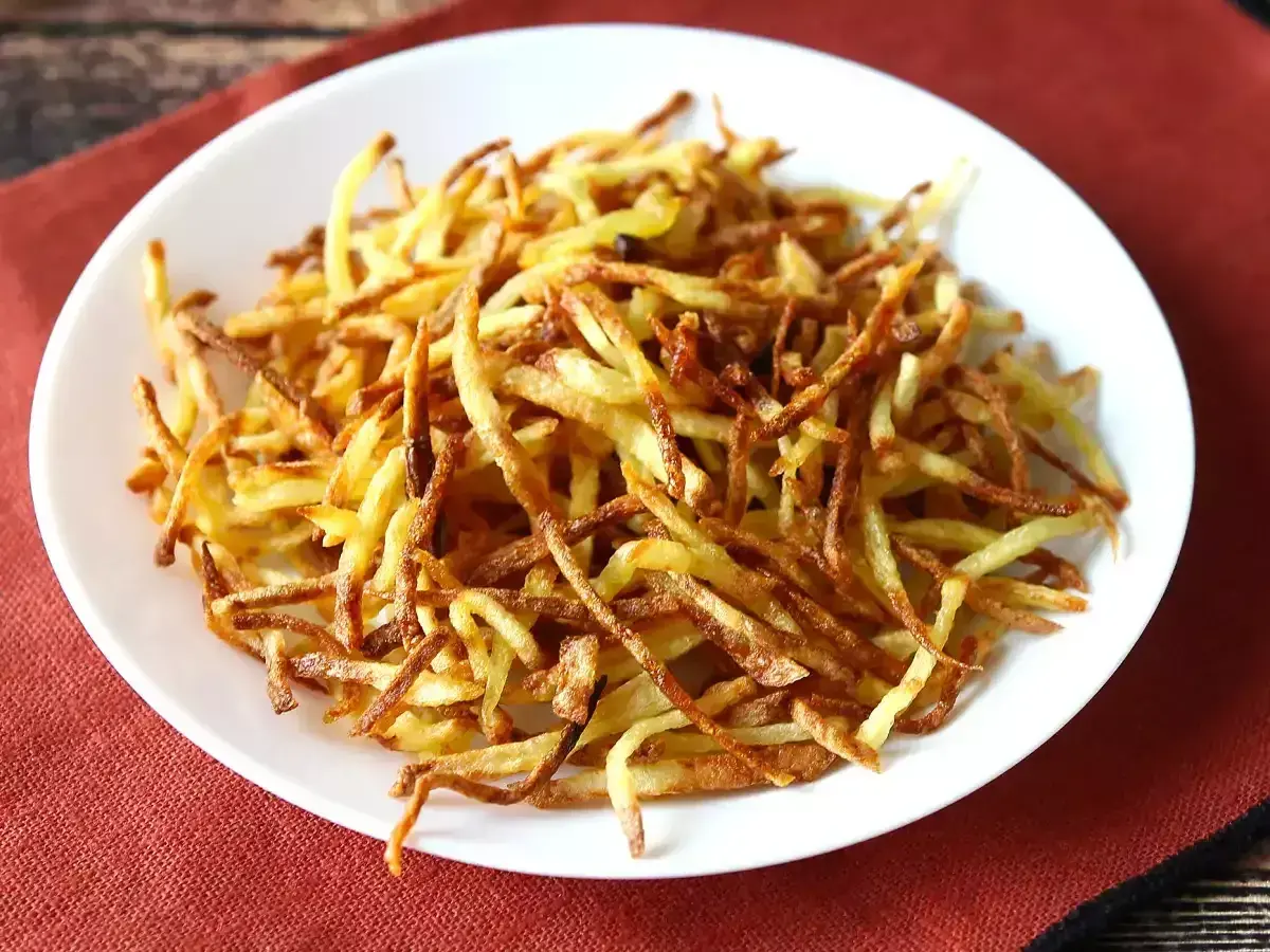 Un plato blanco lleno de crujientes patatas paja doradas, listas para ser disfrutadas.