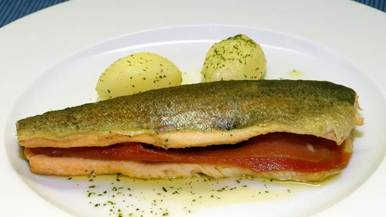 Trucha a la navarra rellena de jamón, servida con patatas cocidas y perejil picado.