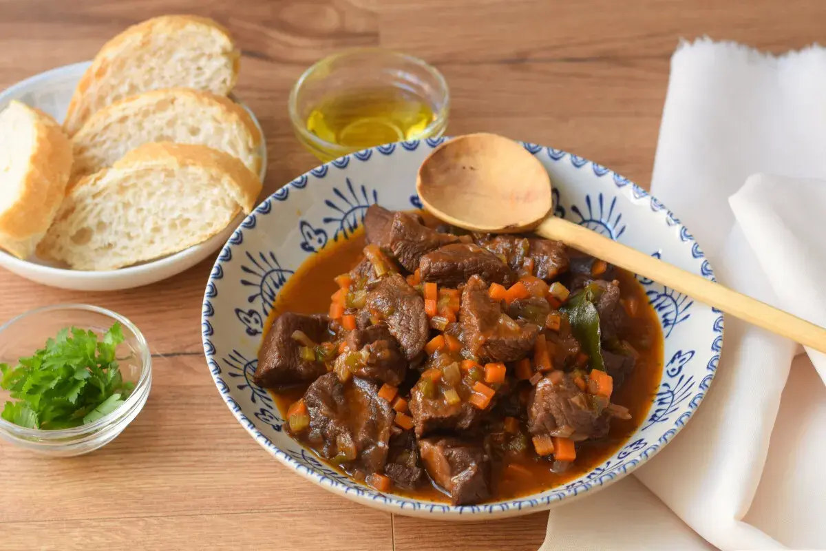 Un reconfortante plato de ternera en salsa, con trozos tiernos de carne, zanahoria y apio, servido con pan y perejil fresco.