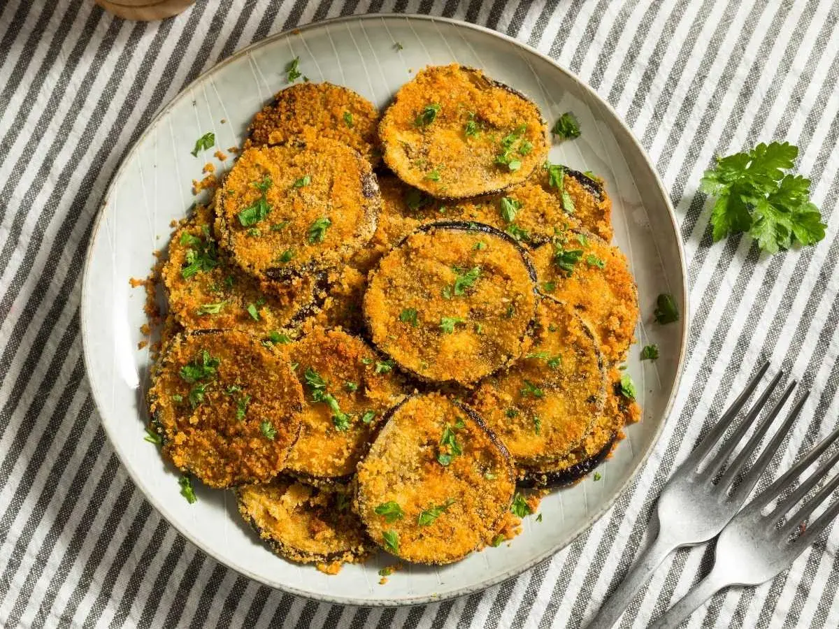 Plato de berenjenas rebozadas, doradas y crujientes, espolvoreadas con perejil fresco.