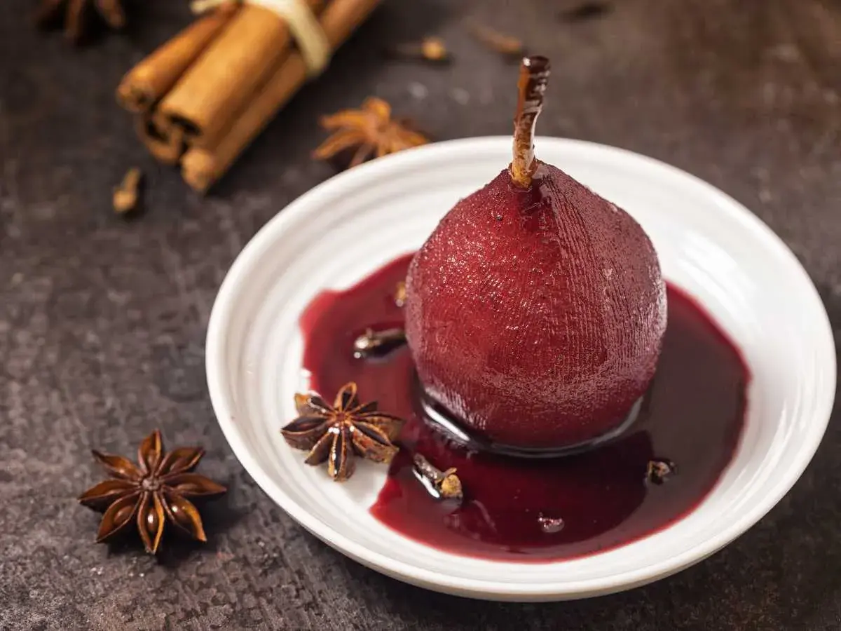 Peras al vino, cocinadas a la perfección, servidas en un plato blanco con especias como anís estrellado y canela.