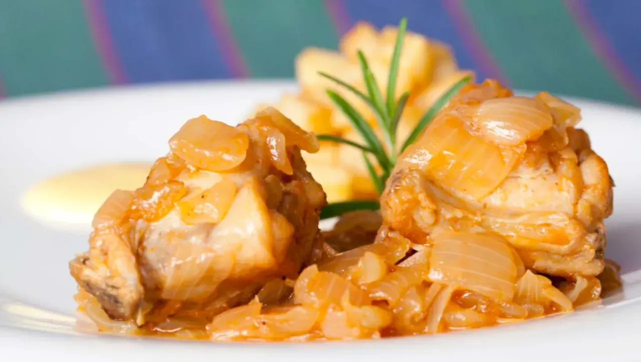 Dos trozos de conejo en escabeche, cubiertos de cebolla caramelizada, acompañados de patatas fritas y una ramita de romero.