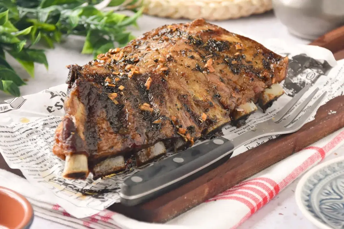 Costillas de churrasco de cerdo glaseadas, servidas sobre papel con texto y acompañadas de un tenedor y cuchillo.
