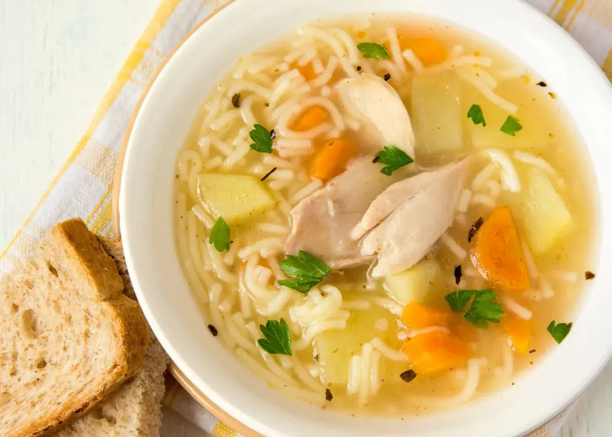 Un reconfortante plato de sopa de pollo receta, con fideos finos, trozos de pollo, patatas y zanahorias, adornado con perejil fresco.