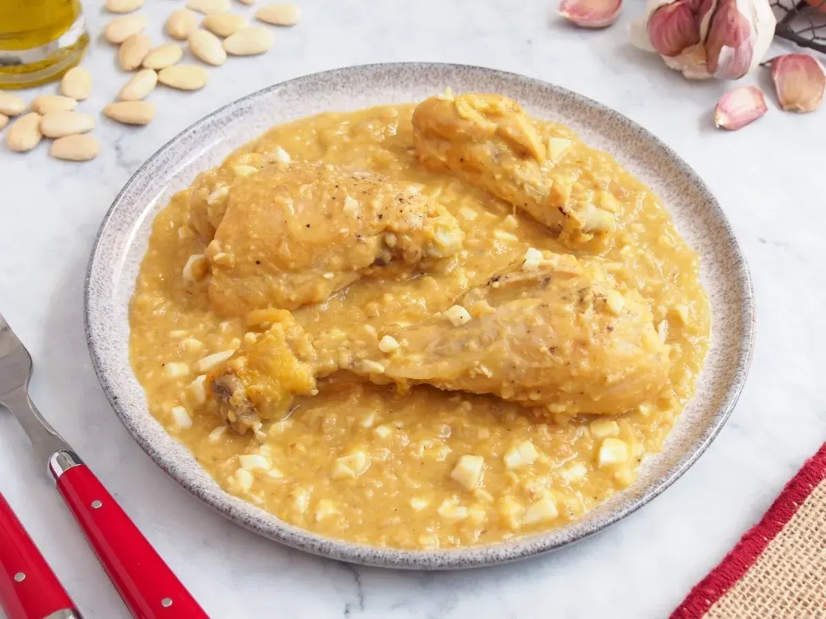 Pollo a la pepitoria servido en un plato, con trozos de huevo duro y almendras esparcidas.