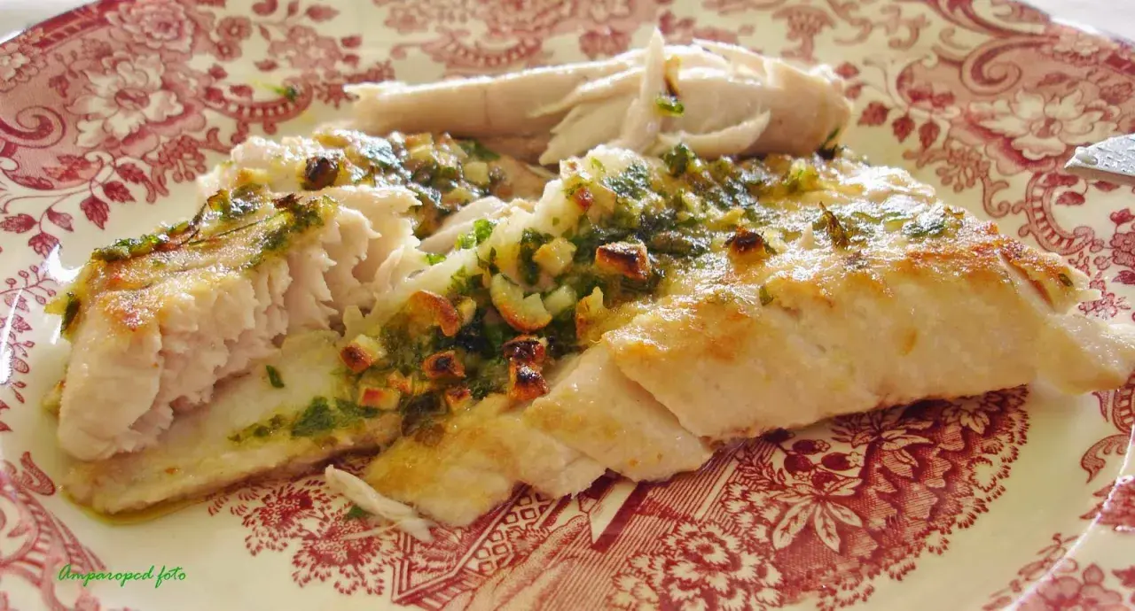 Deliciosa ventresca al horno, jugosa y dorada, con un aderezo verde de hierbas y ajo.