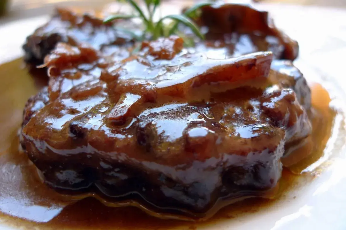 Plato de rabo de toro estofado, con una salsa oscura y brillante, adornado con una ramita de romero.
