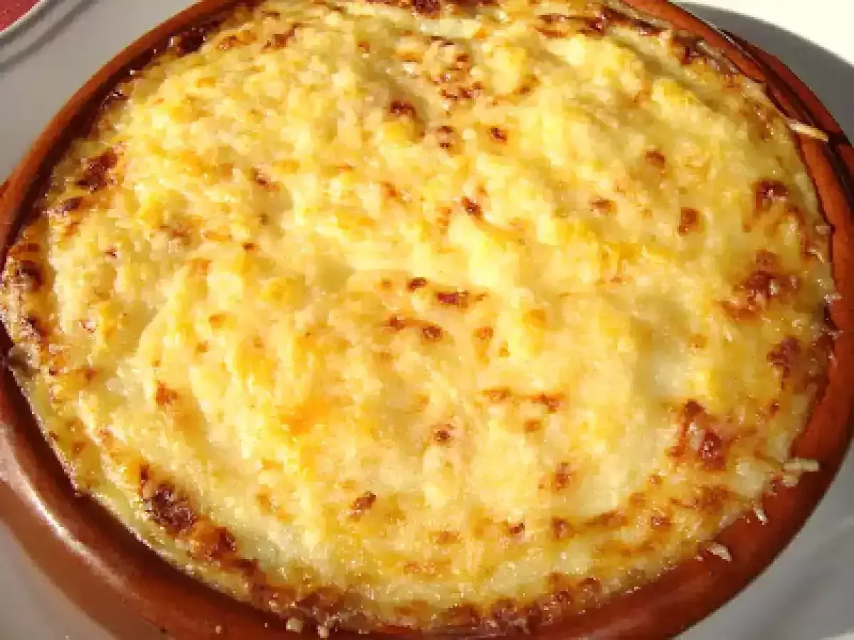 Un delicioso pure de patata gratinado, con bordes dorados y burbujeante, servido en una cazuela de barro.